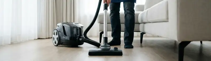Professional house cleaner vacuuming a living room floor with a canister vacuum cleaner, Bradenton, FL.