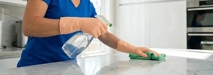 Maid service worker spraying and wiping a kitchen countertop with a microfiber cloth for sanitizing, Bradenton, FL.