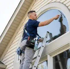Professional window cleaner on a ladder using a squeegee to clean an exterior arched window, Bradenton, FL.