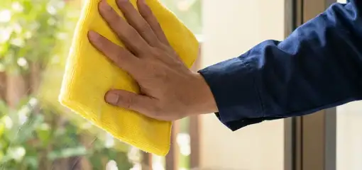 House cleaner wiping a glass window with a yellow microfiber cloth for streak-free cleaning, Bradenton, FL.